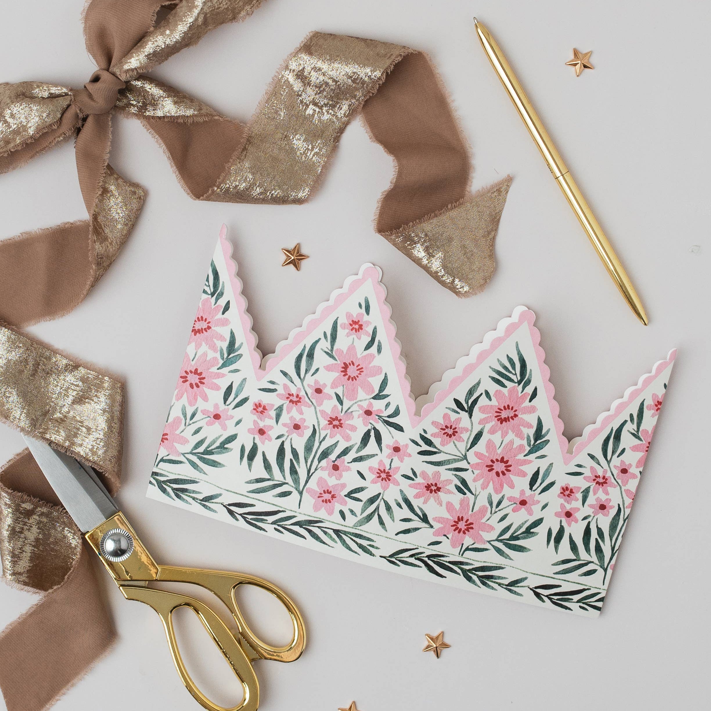 Floral-patterned paper crown with gold scissors and ribbons on a light background