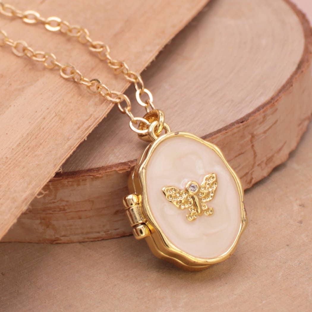 Gold locket necklace with a cream-colored oval pendant featuring a gold butterfly design, resting on a rustic wooden slice.