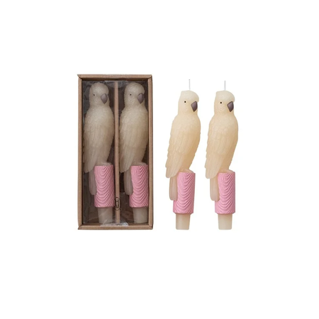 Two parrot-shaped candles with pink bases in a box on a white background