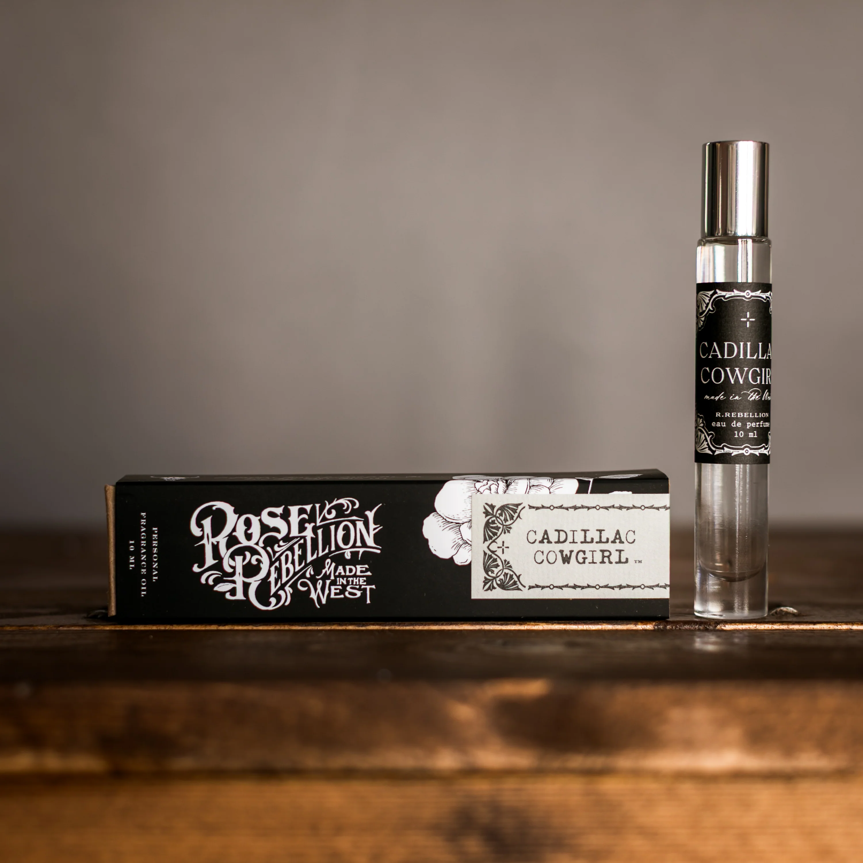 roller ball perfume called cadillac cowgirl with black box packaging on a wood backdop