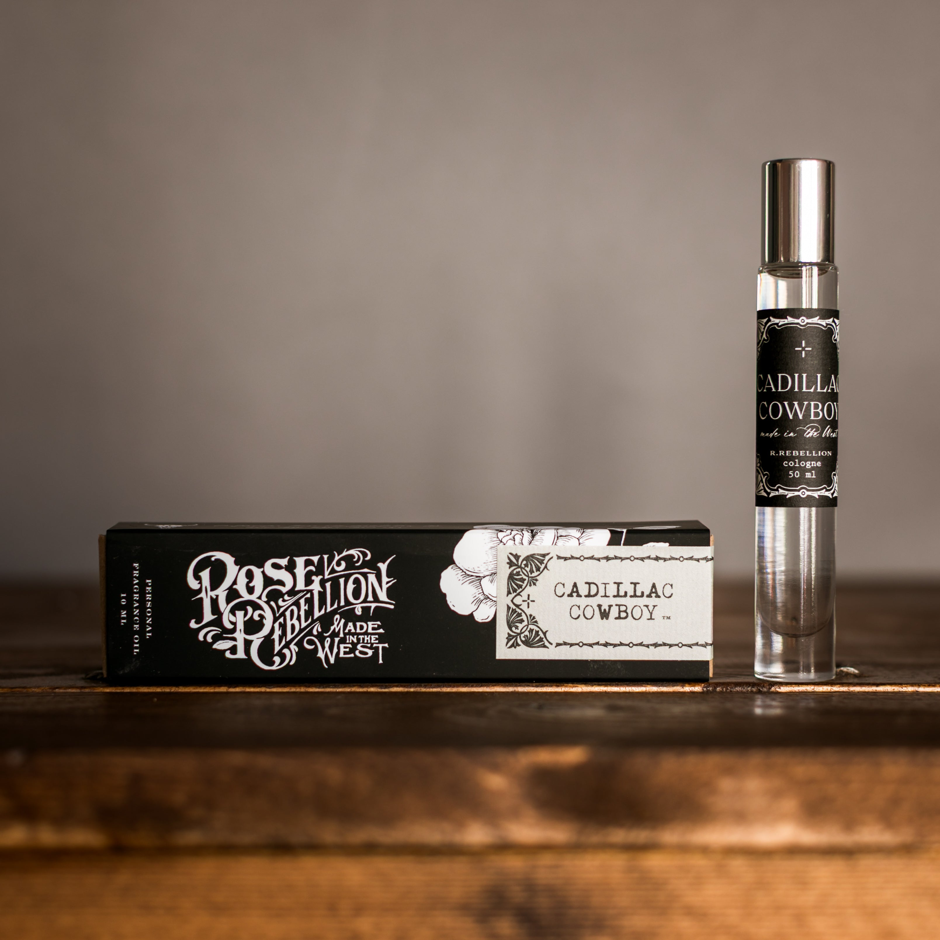 Perfume bottle and packaging labeled 'Cadillac Cowboy' on a wooden surface with a gray background