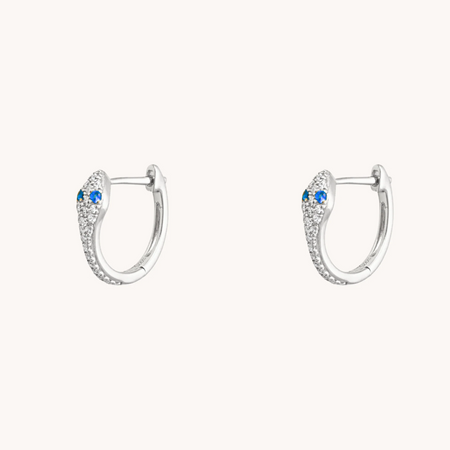 Silver snake huggie earrings with blue sapphire eyes and sparkling accents on a white background.