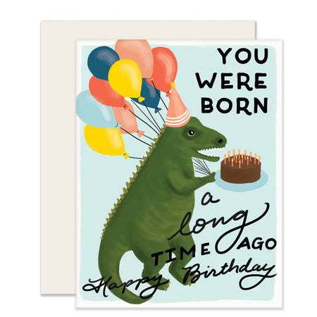 birthday card with dino holding balloons and a birthday cake on a blue background. Reads "you were born, a long time ago. happy birthday"