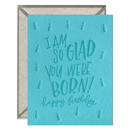 A greeting card with a blue background, featuring white hand-drawn text that reads 'I am so glad you were born!' and additional text that reads 'Happy Birthday!'.