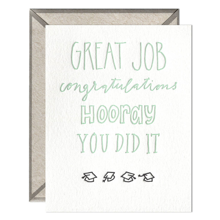 letterpress card that reads "great job, congratulations, hooray, you did it" in green ink with grad caps below the words on a white background