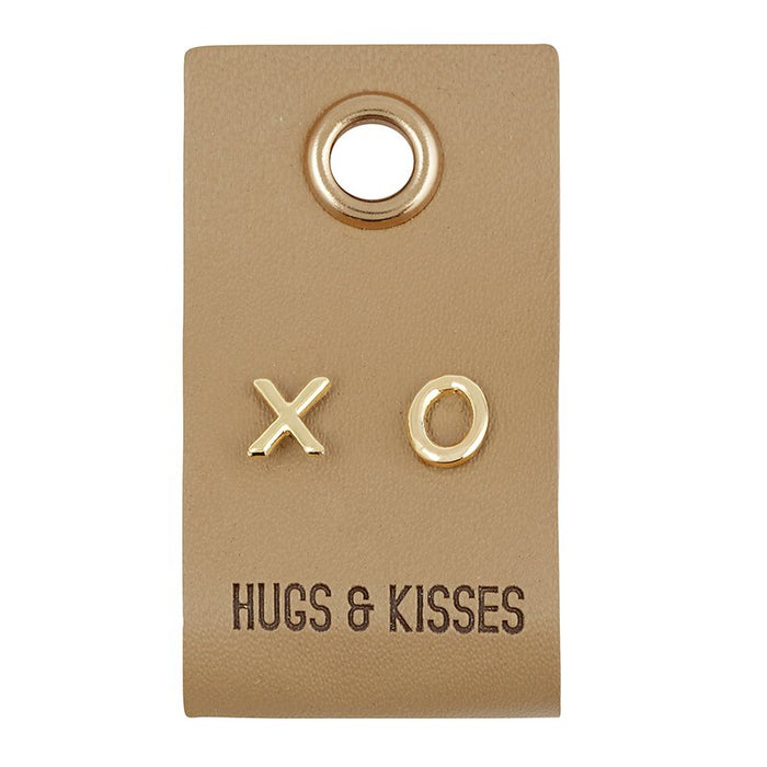 Leather tag with X and O earrings on them. The tag says Hugs & kisses and it is on a white background
