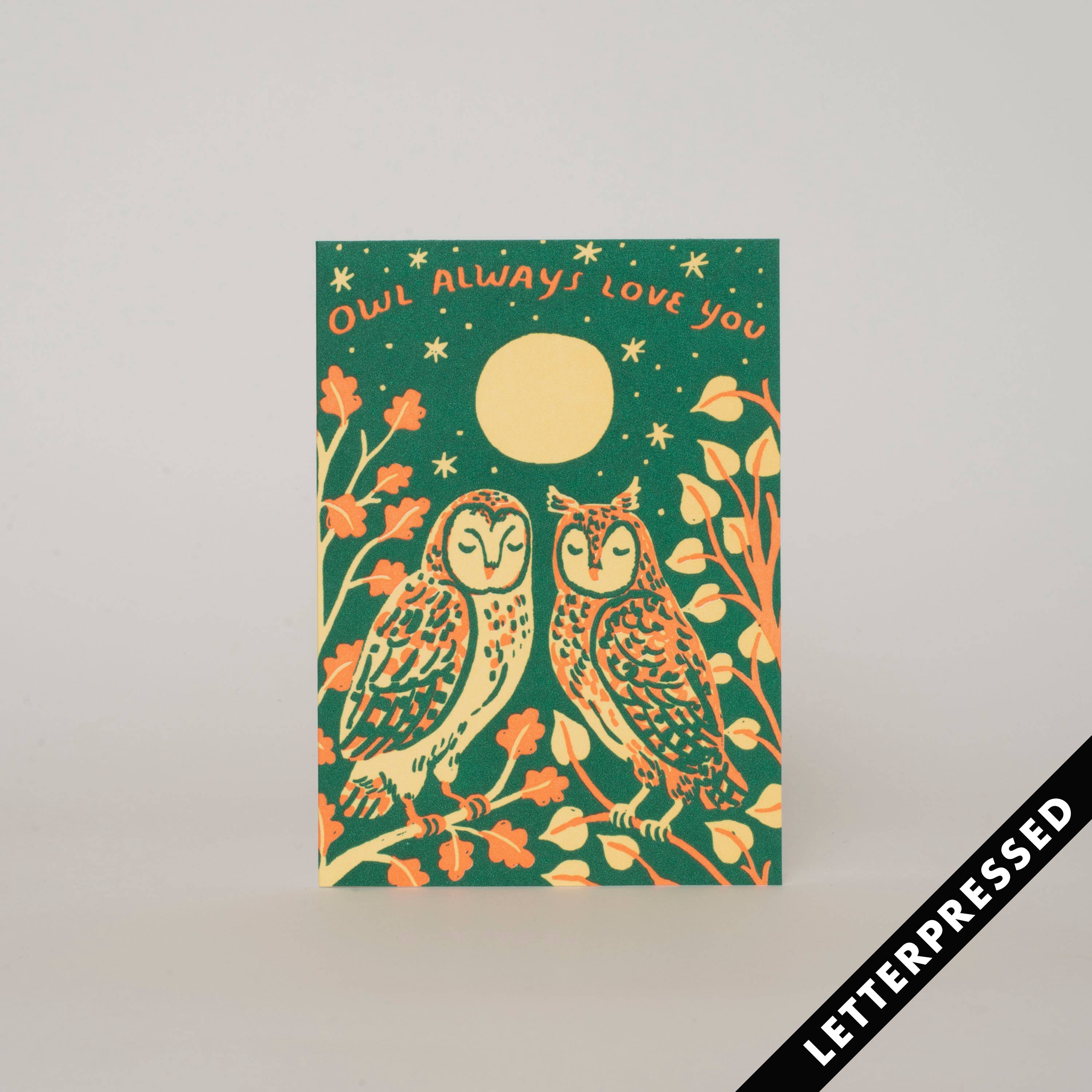 A greeting card with a green background featuring illustrations of two owls, flowers, and a moon. The text on the card reads 'Owl always loves you'.