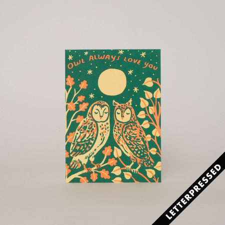 A greeting card with a green background featuring illustrations of two owls, flowers, and a moon. The text on the card reads 'Owl always loves you'.